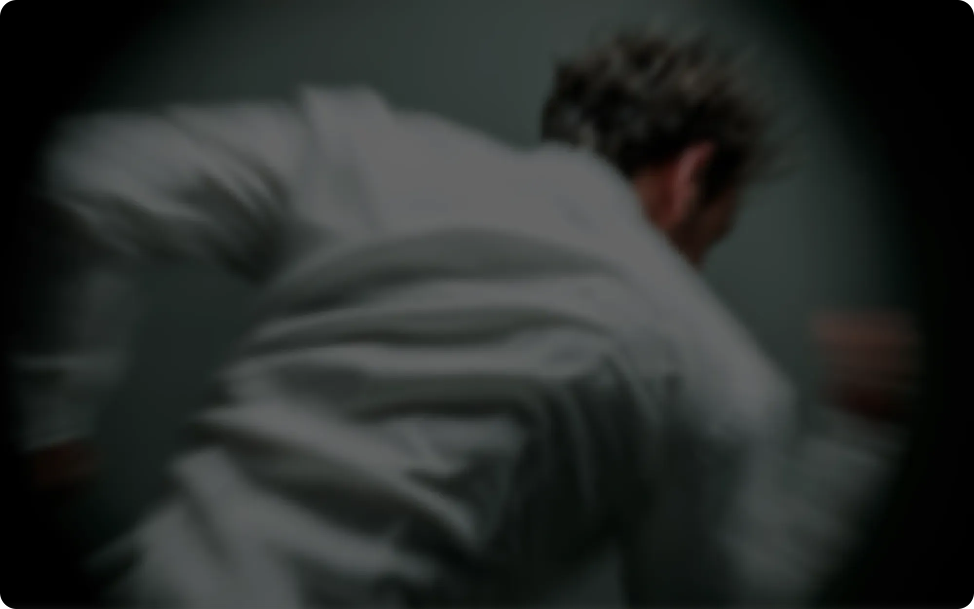 Low-lit editorial scene, a still figure in a wide dark space