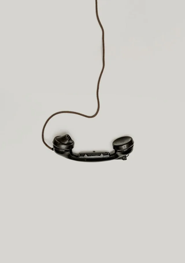 A vintage black telephone handset hanging by its cord against a plain wall